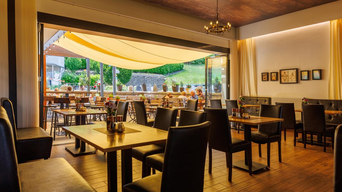 Ein gemütliches Restaurant mit Holzfußboden und eleganten Tischen. Große Fenster bieten einen Blick ins Grüne und lassen viel Tageslicht herein. | © Linshalm Fotografie