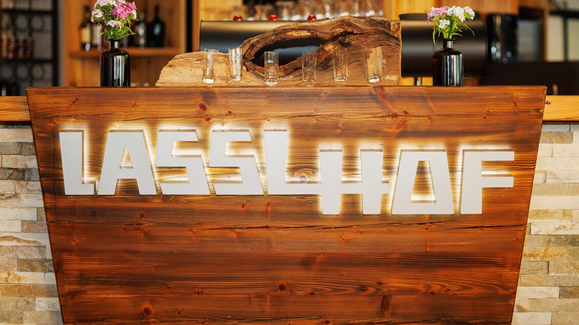 Ein rustikaler Empfangstresen aus Holz mit der Beschriftung "Lasslhof". Auf dem Tresen stehen kleine Blumenvasen. | © Linshalm Fotografie