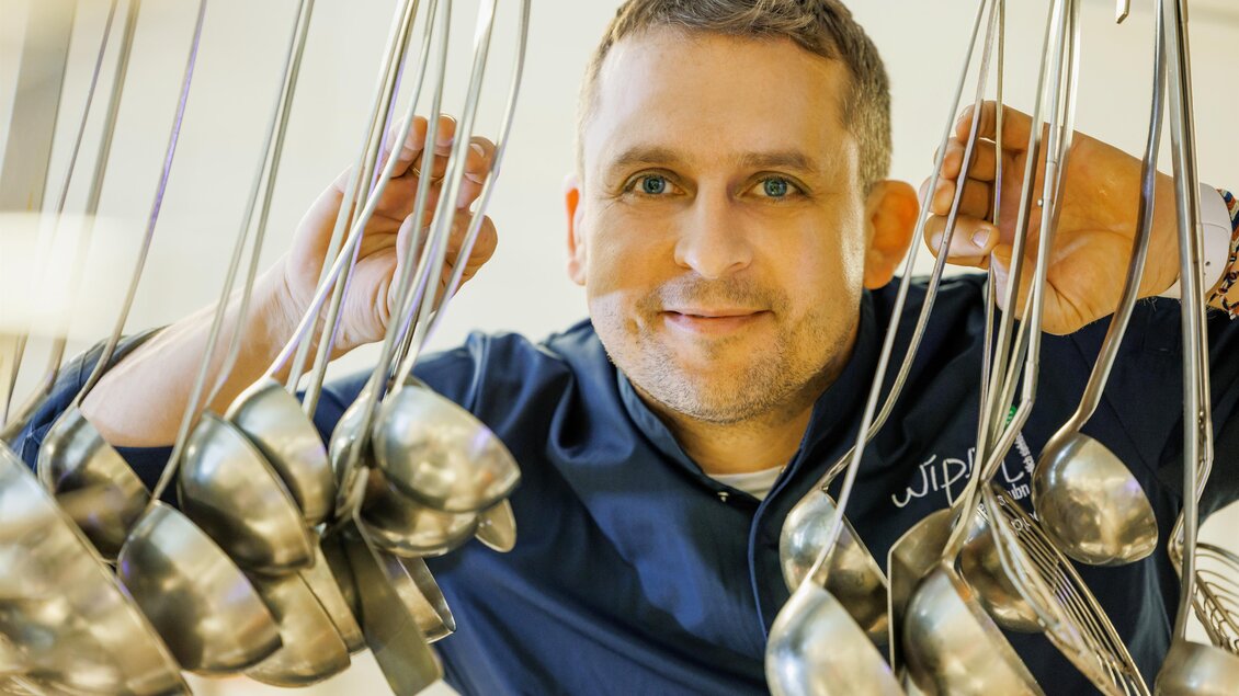 Ein lächelnder Koch steht in einer Küche, umgeben von Kochutensilien. Er präsentiert seine Leidenschaft für das Kochen und die Gastronomie. | © © Linshalm Fotografie