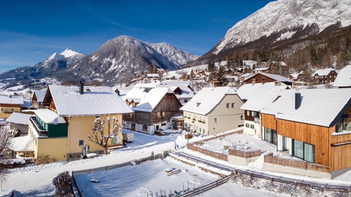 Ein malerisches Dorf im Schnee, umgeben von Bergen. Die Häuser sind mit einer dicken Schneeschicht bedeckt und das Wetter ist klar und sonnig. | © Wirtshaus &amp; Dorfhotel Mayer 