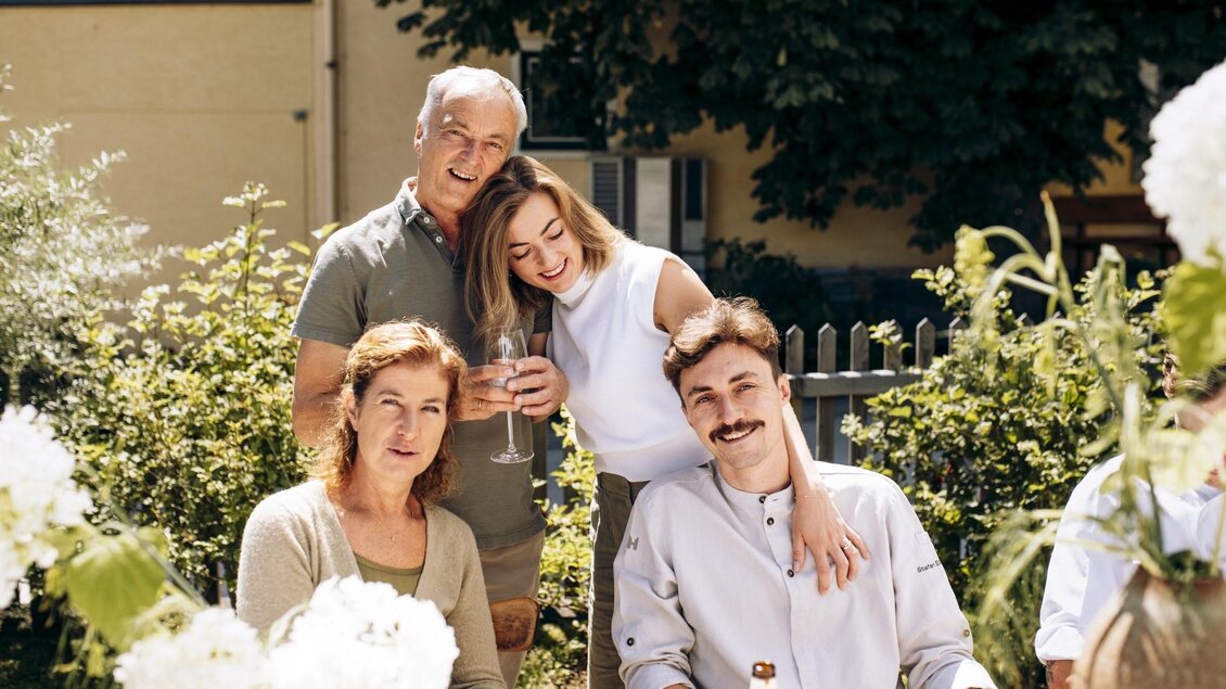 Eine fröhliche Gruppe von vier Personen sitzt im Freien umgeben von Blumen. Sie genießen einen entspannten Moment in einem sonnigen Garten. | © Tobias Müller