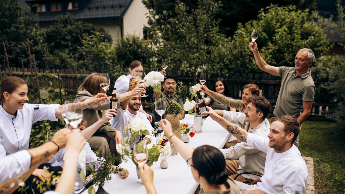 Eine Gruppe von Menschen feiert bei einem Festessen im Freien. Sie stoßen mit Gläsern an und genießen die gemeinsame Zeit in einer schönen Umgebung. | © Tobias Müller