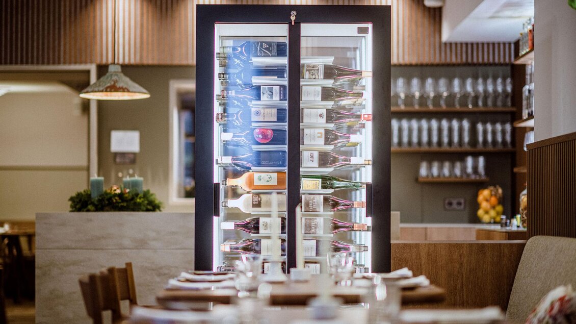 Ein modernes Restaurant mit einem eleganten Weinregal im Hintergrund. Die Tische sind schön gedeckt und die Atmosphäre ist einladend. | © Wein