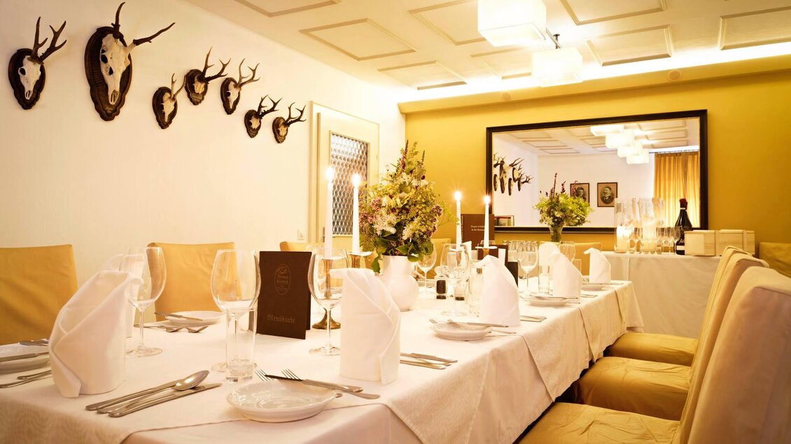 Ein elegantes Restaurant mit einem gedeckten Tisch und hochwertigen Tischen. An der Wand hängen Hirschgeweihe und das Ambiente ist gemütlich. | © Friedrich