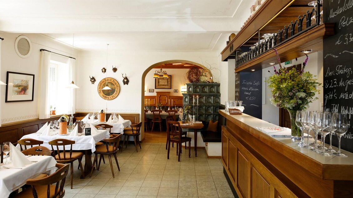 Ein gemütliches Restaurant mit Holzmöbeln und Tischen, die schön gedeckt sind. Im Hintergrund gibt es eine Bar mit Gläsern und einer Tafel mit Speisen. | © Friedrich Andreas