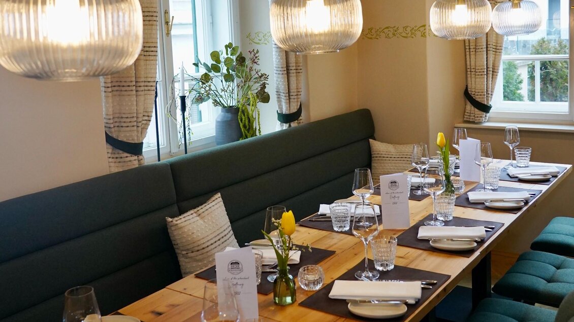 Elegant gedeckter Tisch mit Gläsern, Menükarten und Blumen im hellen Restaurantbereich des Schanzlwirt Graz | © Wirtshaus Schanzlwirt