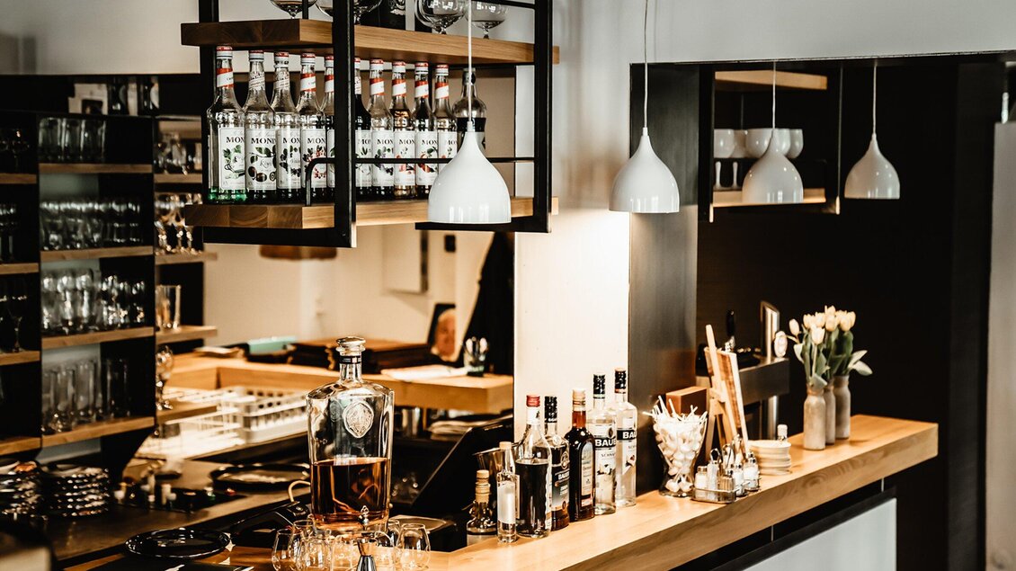 Eine moderne Bar mit einer Holztheke, Gläsern und verschiedenen Spirituosen. Die Einrichtung ist stilvoll mit warmen Lichtquellen und dekorativen Elementen. | © Wirtshaus Thorbauer - Julian Wallner