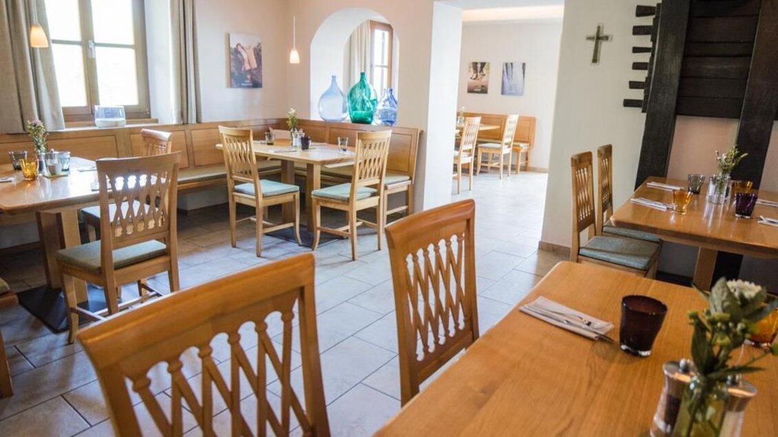 Ein gemütliches Restaurant mit Holztischen und Stühlen. Der Raum ist hell und einladend, mit Kunstwerken an den Wänden. | © Magdalena Koinegg