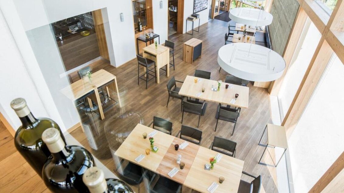 Ein modernes Restaurant mit Holztischen und schwarzen Stühlen. Viel Licht fällt durch große Fenster und schafft eine einladende Atmosphäre. | © Magdalena Koinegg