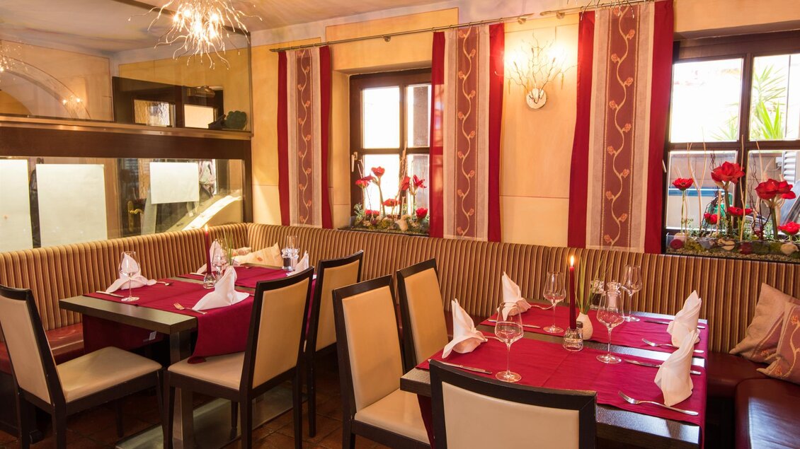 Ein gemütliches Restaurant mit eleganten Tischen und roten Tischdecken. Die Wände sind mit schönen Pflanzen und dekorativen Elementen geschmückt. | © Restaurant Haider