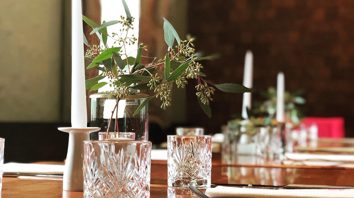 Ein eleganter Tisch mit zarten Blumen in einer Glasvase. Im Hintergrund sind Kerzen und ein stilvolles Ambiente sichtbar. | © Landhotel am Gut Moser | Familie Kapun