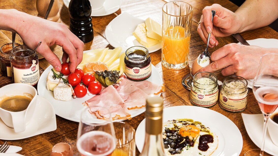 Ein festlicher Tisch mit verschiedenen Speisen, einschließlich Käse, Wurst, frischen Tomaten und Marmelade. Getränke wie Säfte und Kaffee sind ebenfalls auf dem Tisch zu sehen. | © Landhotel am Gut Moser | Familie Kapun