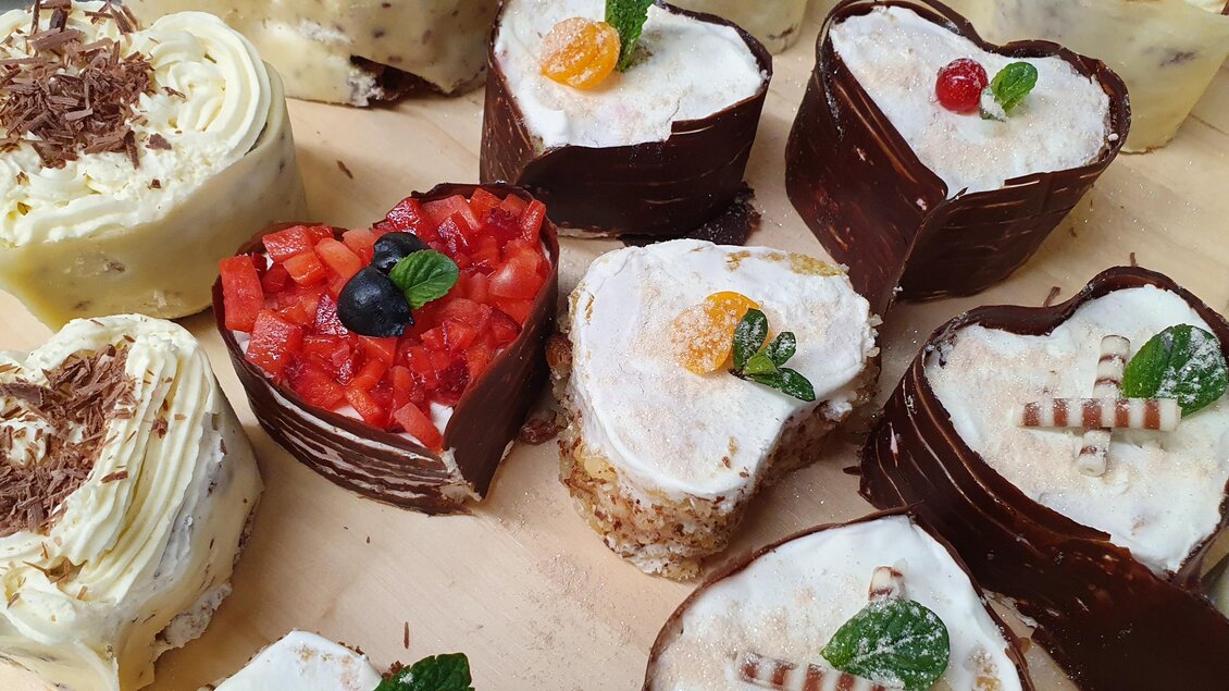 Eine Auswahl an herzförmigen Törtchen mit verschiedenen Belägen und Dekorationen. Die Törtchen sind farbenfroh und ansprechend angerichtet.