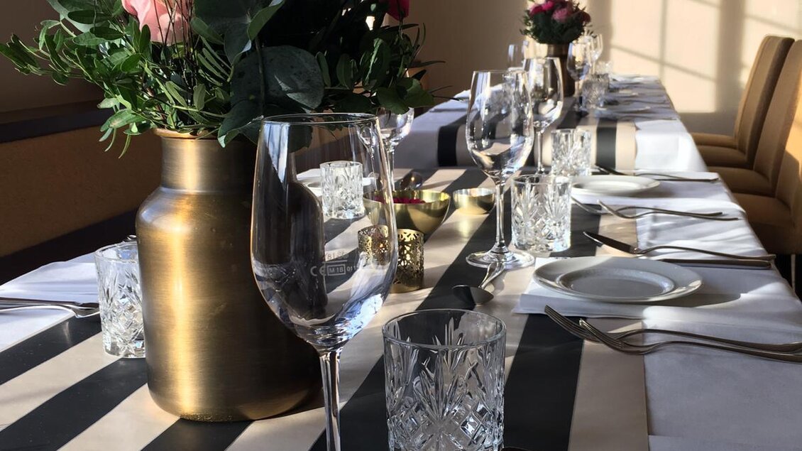 Ein elegant dekorierter Tisch mit Blumenarrangement und Gläsern. Die Sonnenstrahlen scheinen durch das Fenster und schaffen eine angenehme Atmosphäre. | © Landhotel am Gut Moser | Familie Kapun