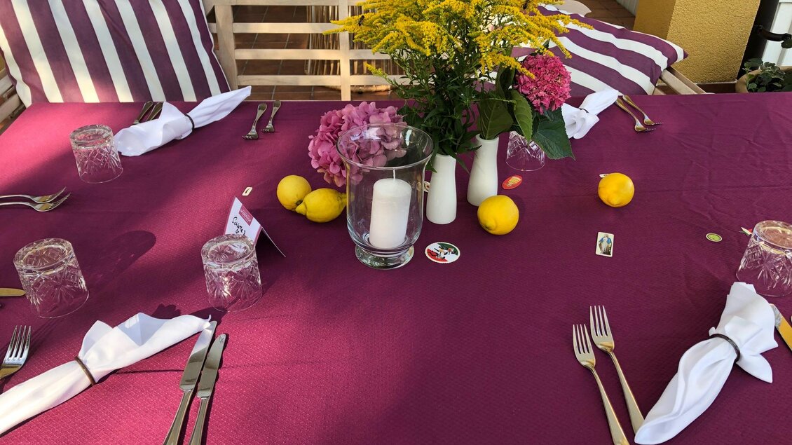 Ein schön gedeckter Tisch mit einem lila Tischdecke, Gläsern und Besteck. In der Mitte stehen frische Blumen und einige Zitronen. | © Landhotel am Gut Moser | Familie Kapun