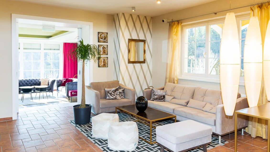 Ein modernes Wohnzimmer mit einer hellen Couch, einem Couchtisch und einem stilvollen Teppich. Große Fenster sorgen für viel Licht und eine einladende Atmosphäre.