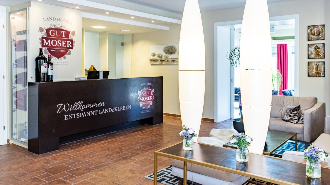 Eine moderne Hotelrezeption mit einem eleganten Empfangstresen. Im Hintergrund sind gemütliche Sitzgelegenheiten und dekorative Elemente zu sehen.