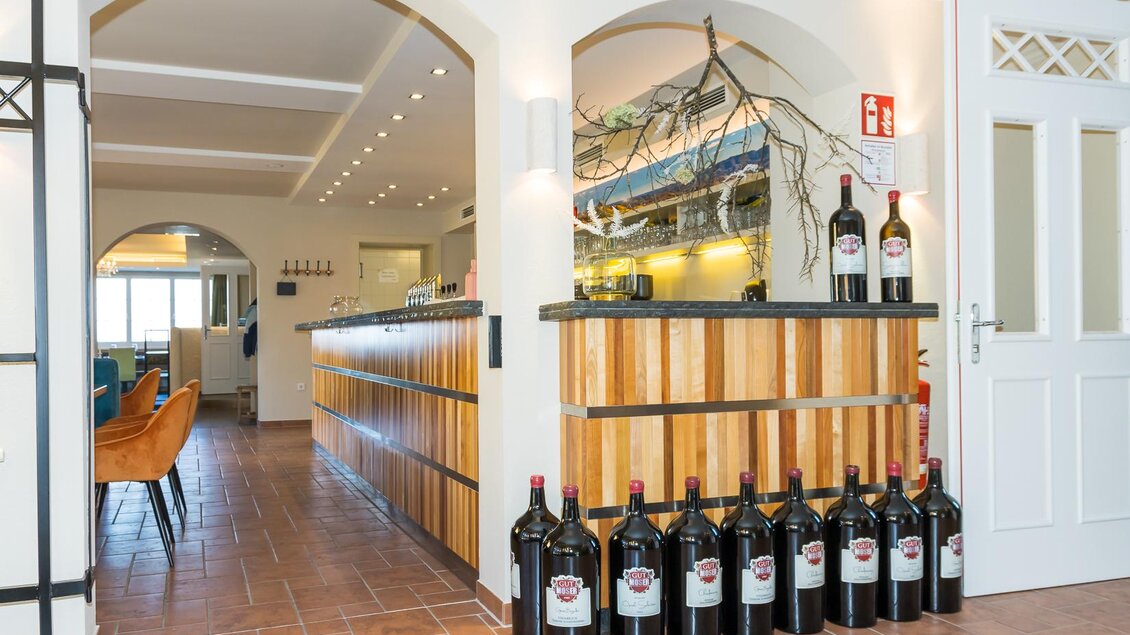 Ein modernes Restaurant mit einem eleganten Tresen aus Holz. Im Hintergrund sind Weinfässer und eine gemütliche Atmosphäre zu sehen.