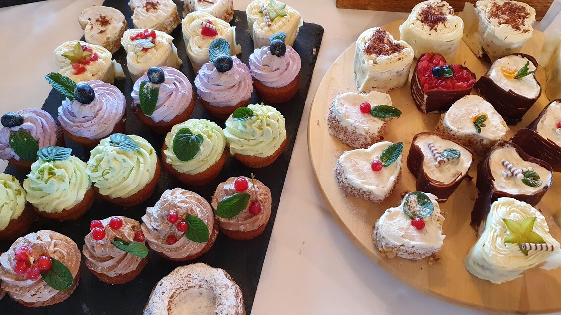 Eine Auswahl an köstlichen Cupcakes in verschiedenen Farben und Geschmacksrichtungen. Die Dekoration umfasst Früchte und essbare Blätter.