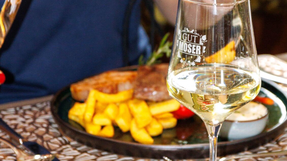 Ein Teller mit Steak, Pommes frites und Gemüse. Daneben steht ein Glas Weißwein.