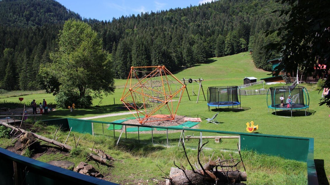 Ein schöner Spielplatz in der Natur mit Klettermöglichkeiten und Trampolinen. Die umliegende Landschaft ist grün und von Bäumen umgeben. | © Viola Lechner