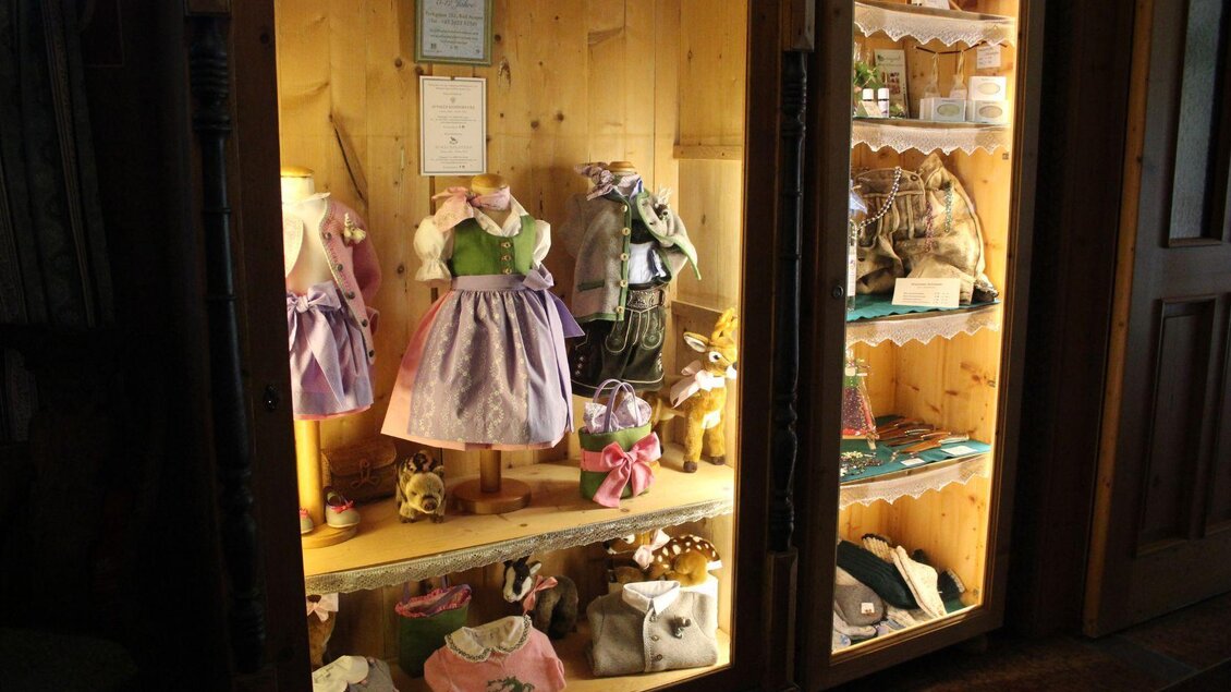 Ein Schaufenster mit handgefertigten Kleidern und Spielzeugen. Die Figuren sind bunt und gut sichtbar in einem Holzregal ausgestellt. | © Viola Lechner