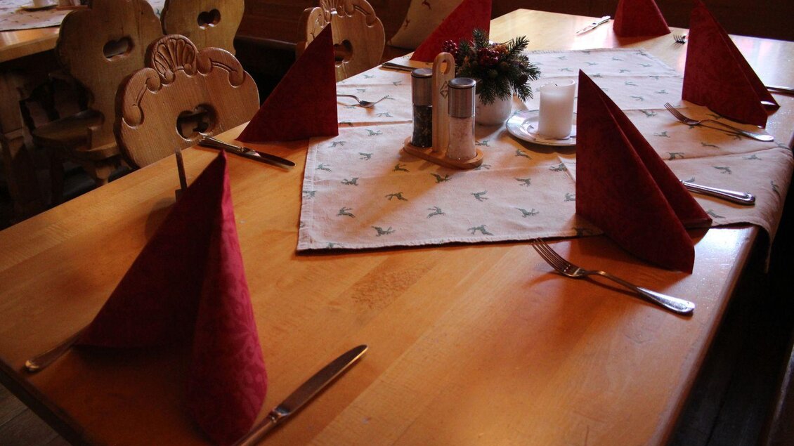 Ein schön gedeckter Tisch mit roten Servietten in einer gemütlichen Atmosphäre. Die Holzstühle und das Tischdecken-Design verleihen dem Raum ein rustikales Ambiente. | © Viola Lechner