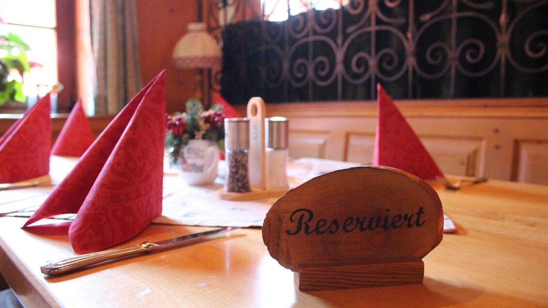 Ein gedeckter Tisch mit roten Servietten und einem Holzschild mit der Aufschrift „Reserviert“. Der Tisch ist in einem gemütlichen Restaurant dekoriert. | © Viola Lechner