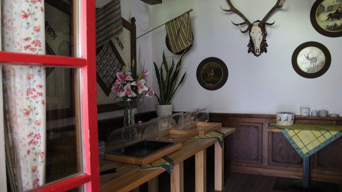 Ein gemütlicher Raum mit holzernen Tischen und traditionellen Dekorationen. Blumen und Pflanzen verleihen dem Raum eine einladende Atmosphäre. | © Viola Lechner