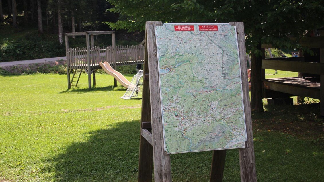 Eine Karte steht auf einem Holzgestell im Grünen. Im Hintergrund sind Spielgeräte und Bäume zu sehen. | © Viola Lechner