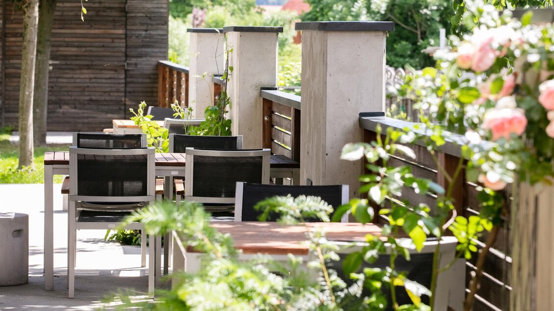 Ein einladender Außenbereich mit Tischen und Stühlen. Die Umgebung ist grün und blühend, ideal für entspannte Begegnungen. | © Stainzerhof KG