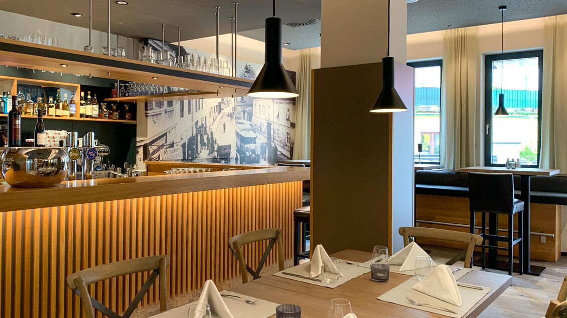 Ein modernes Restaurant mit eleganter Einrichtung und einer Bar im Hintergrund. Tische sind vorbereitet mit weißen Servietten und Glaswaren. | © Stainzerhof KG