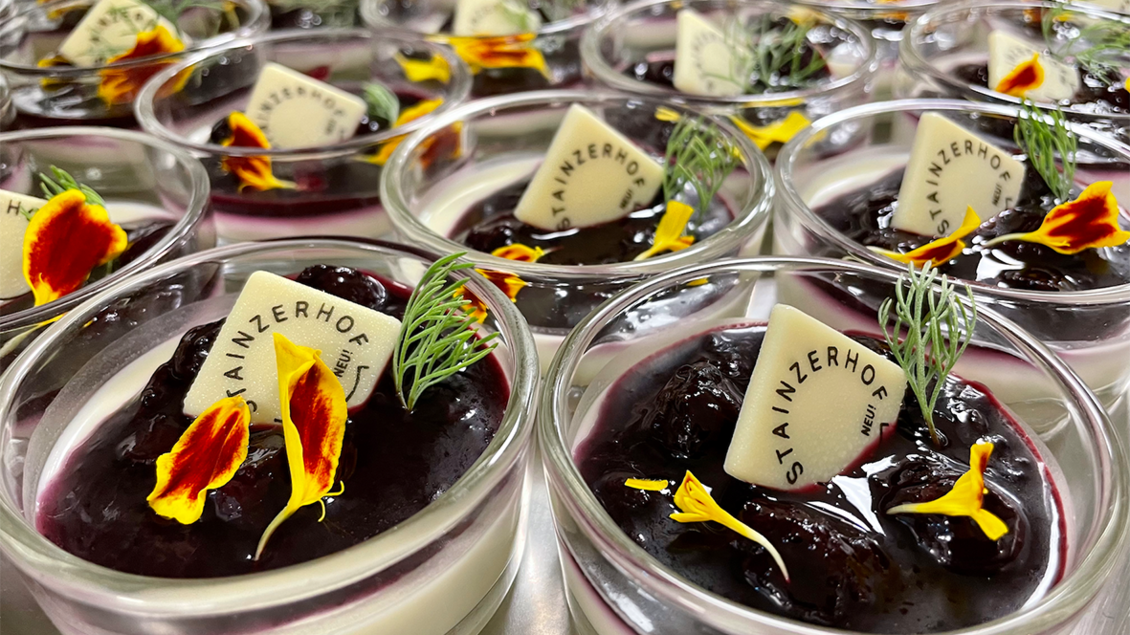 Eine Vielzahl von Dessertgläsern mit einer Schicht Panna Cotta und einer fruchtigen Beerenmasse. Jedes Glas ist mit essbaren Blüten und einer Dekorationskarte versehen. | © Renate Pein