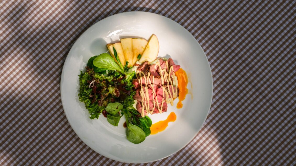 Ein Teller mit zarter Fleischscheibe, frischem Salat und Apfelscheiben. Die Anrichtung ist kreativ und ansprechend. | © Robert Bodnar