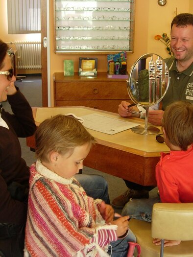 A man advises a family in an optician's shop. The mother is sitting with sunglasses, while the children are listening attentively. | © Wutscher Optik