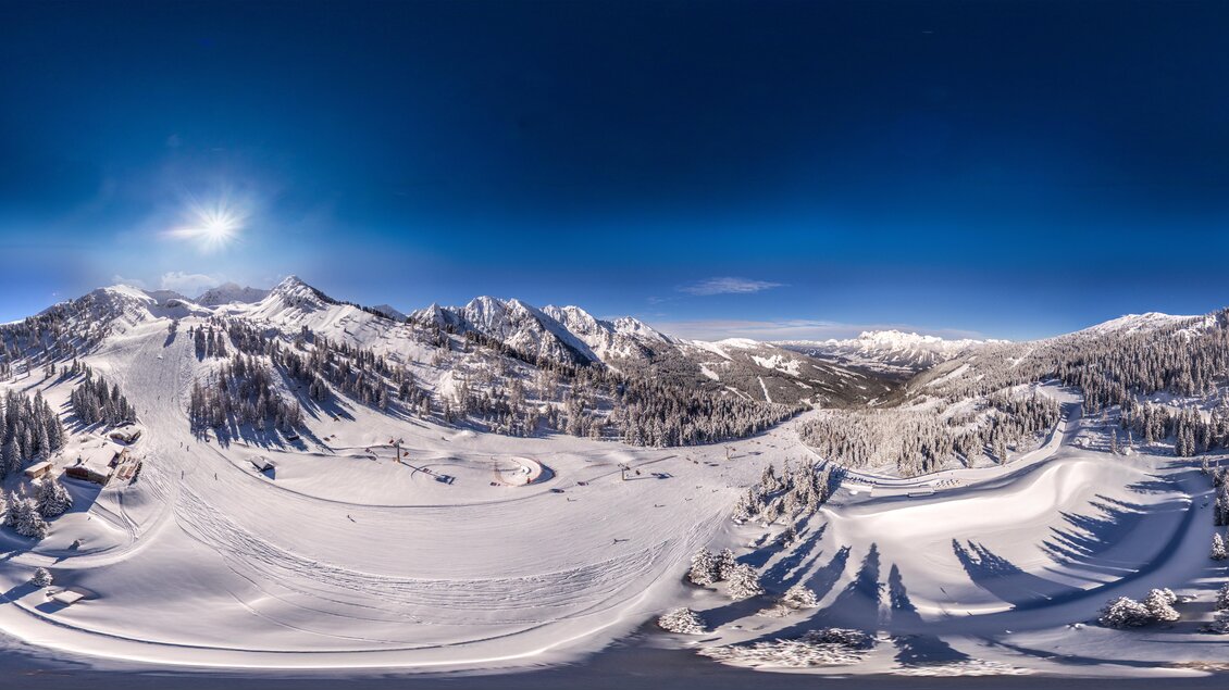 Eine malerische Winterlandschaft mit schneebedeckten Bergen und strahlend blauem Himmel. Skifahrer genießen die Pisten in der Stille der Natur. | © Hauser Kaibling
