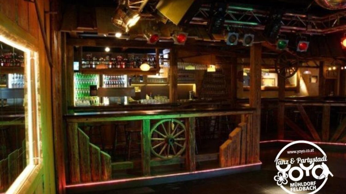 Eine rustikale Bar mit holzverkleideten Wänden und bunten Lichtern. Der Raum hat eine einladende Atmosphäre für Tanz und Partys. | © Yoyo Feldbach