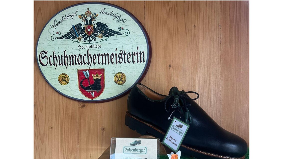 Ein traditioneller Schuh aus Leder, neben einer Plakette mit der Aufschrift "Schuhmachermeisterin". Die Präsentation zeigt handwerkliche Schuhmacherkunst in einem rustikalen Ambiente. | © TVB Ausseerland Salzkammergut_ Nathalie Schickinger