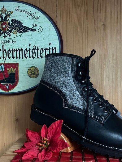Ein handgefertigter Schuh aus Leder und Filz steht auf einem Tisch. Im Hintergrund ist ein Schild mit dem Schriftzug "Schuhmachermeisterin" zu sehen. | © TVB Ausseerland- Salzkammergut_Nathalie Schröttenhamer