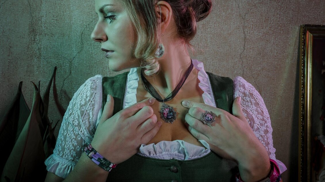 Eine Frau trägt ein traditionelles Outfit mit filigranem Schmuck. Sie posiert seitlich und blickt nachdenklich in die Ferne. | © Fotowerkstatt Irdning, Stefanie Pulsinger