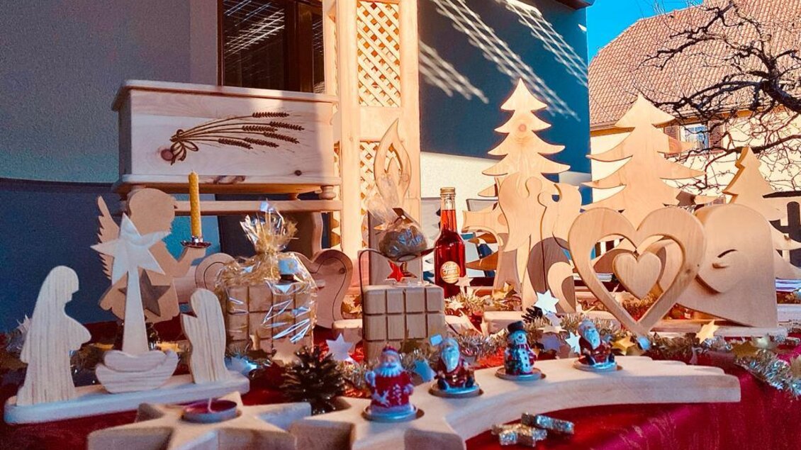 Eine dekorative Holzausstellung mit verschiedenen handgefertigten Figuren, darunter Engel, Weihnachtsbäume und Herzen. Die Szene ist festlich und zeigt handwerkliche Kunstwerke.
