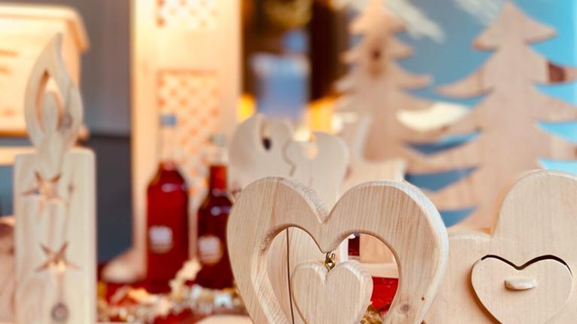 Eine festliche Dekoration mit Holzfiguren in Herz- und Baumform. Auf einem roten Tisch liegen Sterne und andere weihnachtliche Accessoires.