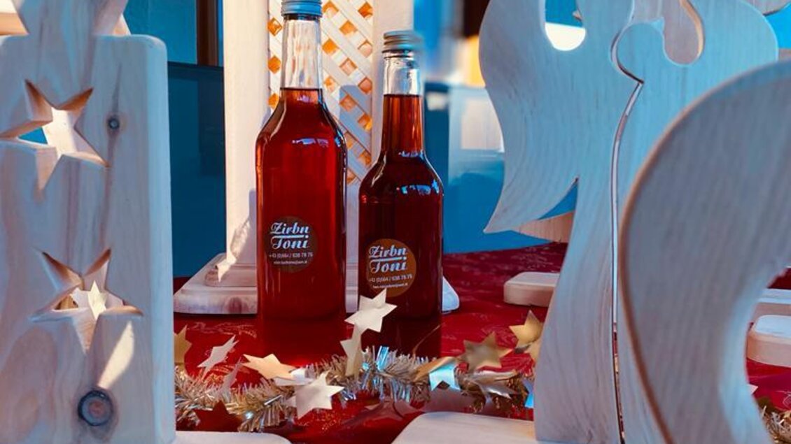 Eine festliche Tischdekoration mit Holzfiguren und zwei Flaschen Getränk. Im Hintergrund sind Weihnachtssterne und eine Tannenzapfen-Dekoration zu sehen.