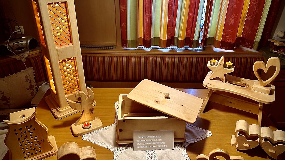 Eine Holzschnitzerei-Ausstellung mit verschiedenen dekorativen Objekten. Im Hintergrund sind farbige Vorhänge zu sehen. | © Zirben Toni