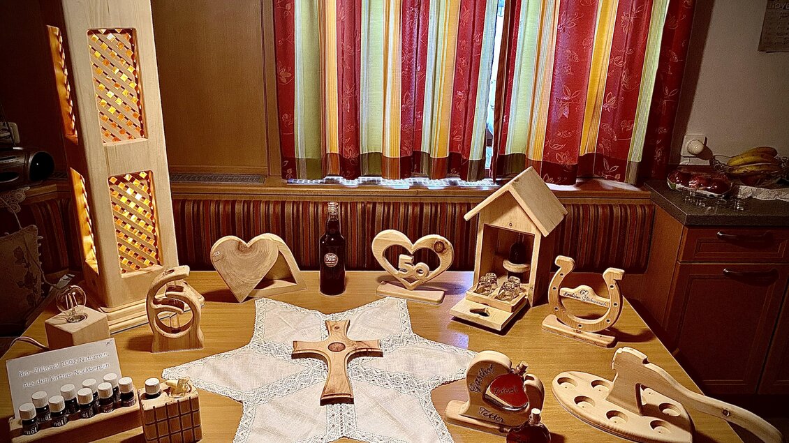 Ein Tisch mit handgefertigten Holzdekorationen, darunter ein Stern, Herzen und eine kleine Vogelhäuschen. Im Hintergrund hängen farbige Vorhänge. | © Zirben Toni