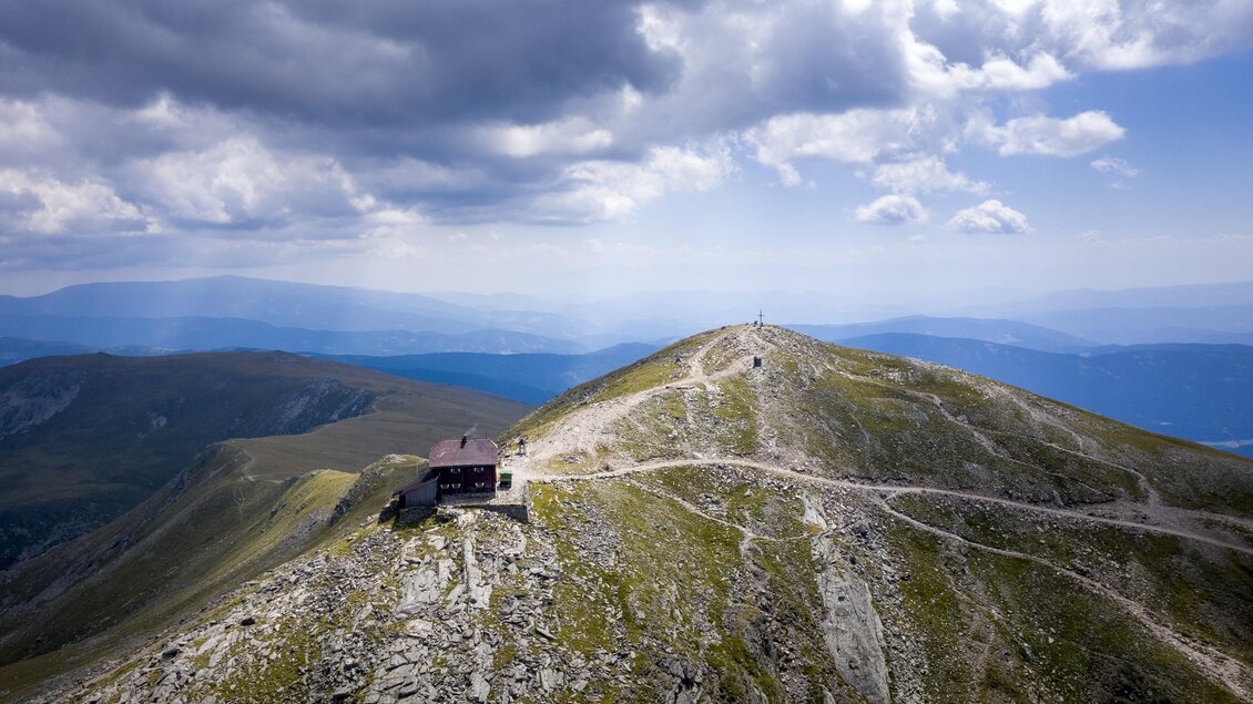 Ein atemberaubender Berggipfel mit einem kleinen Gebäude und einem klaren Himmel. Die Landschaft ist sanft geschwungen und bietet weite Ausblicke auf die umliegenden Berge. | © TVB Murau