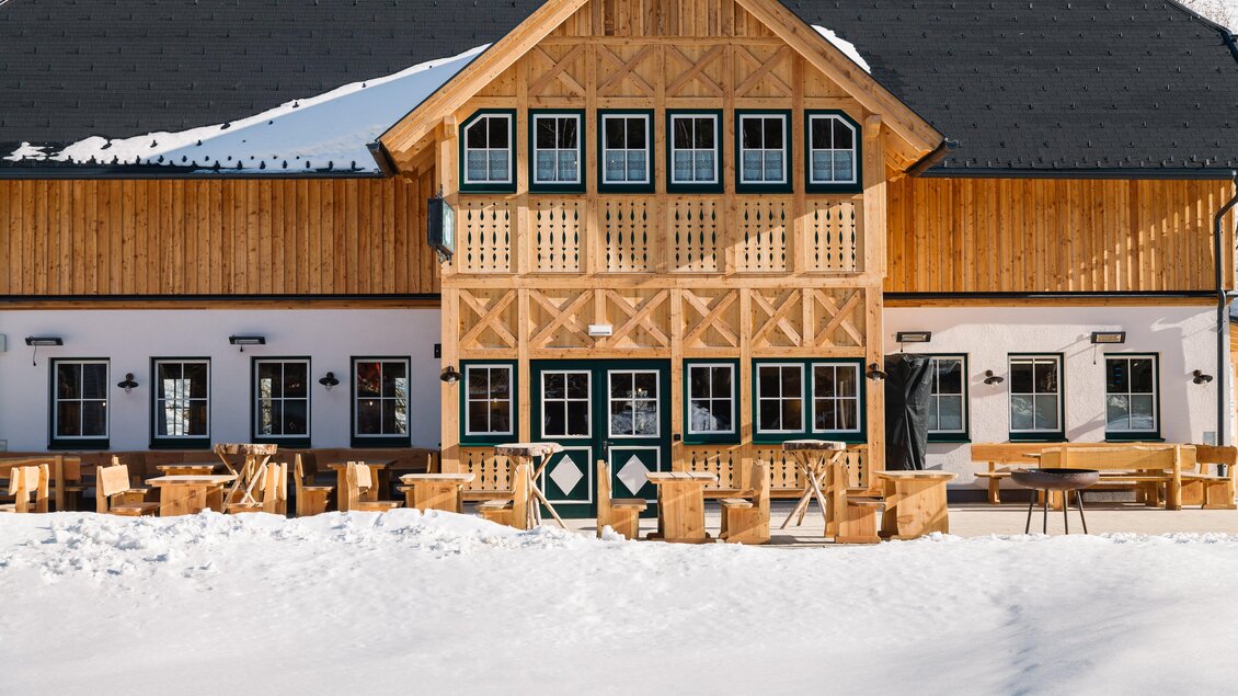 Ein schönes Holzgebäude mit einem traditionellen Design inmitten einer schneebedeckten Landschaft. Vor dem Gebäude stehen rustikale Holzmöbel.