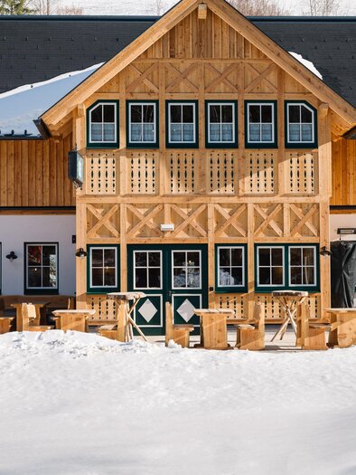 A beautiful wooden building with a traditional design set amidst a snowy landscape. Rustic wooden furniture sits in front of the building.