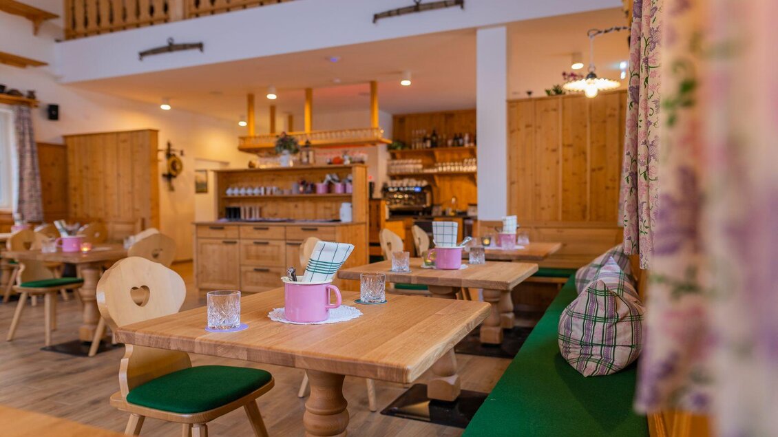 Ein gemütliches Restaurant mit Holzmöbeln und grünem Polster. Die Tische sind liebevoll dekoriert mit pinken Elementen und Blick auf die Theke. | © Narzissendorf Zloam