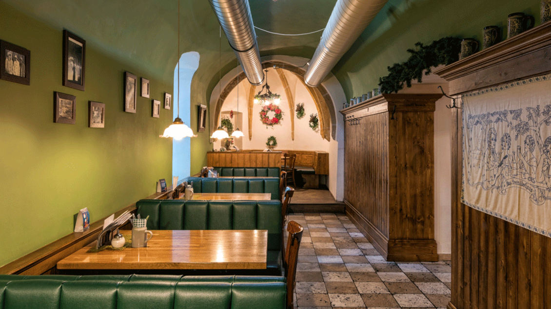 Ein gemütliches Restaurant mit grünen Sitzbänken und Holzmöbeln. An den Wänden hängen Bilder und es gibt eine festliche Dekoration. | © Zu den 3 goldenen Kugeln